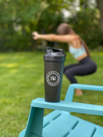 Black Shaker Cup sitting on chair with woman squatting in background